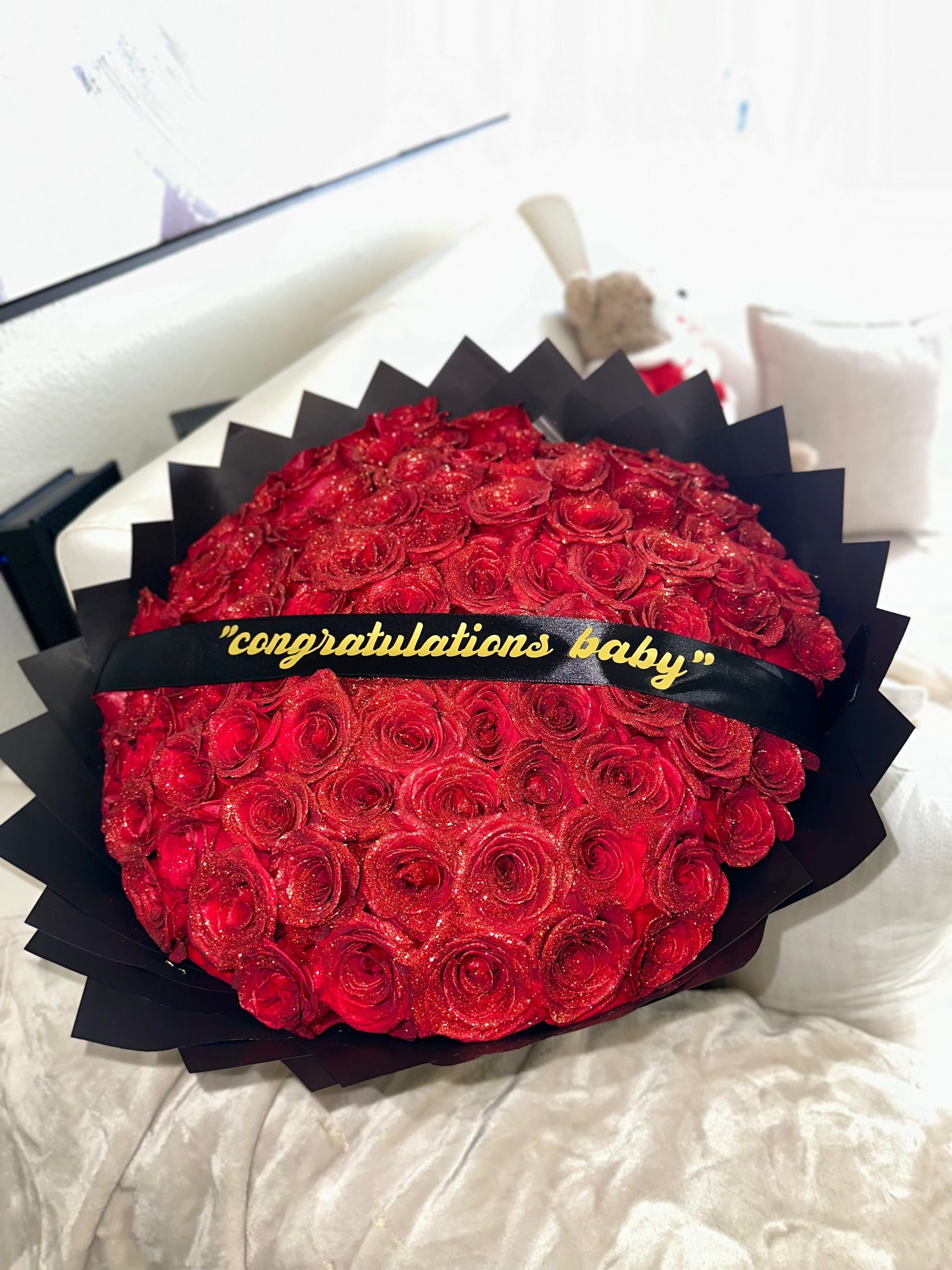 A bouquet of red roses with a black ribbon that says congratulations baby