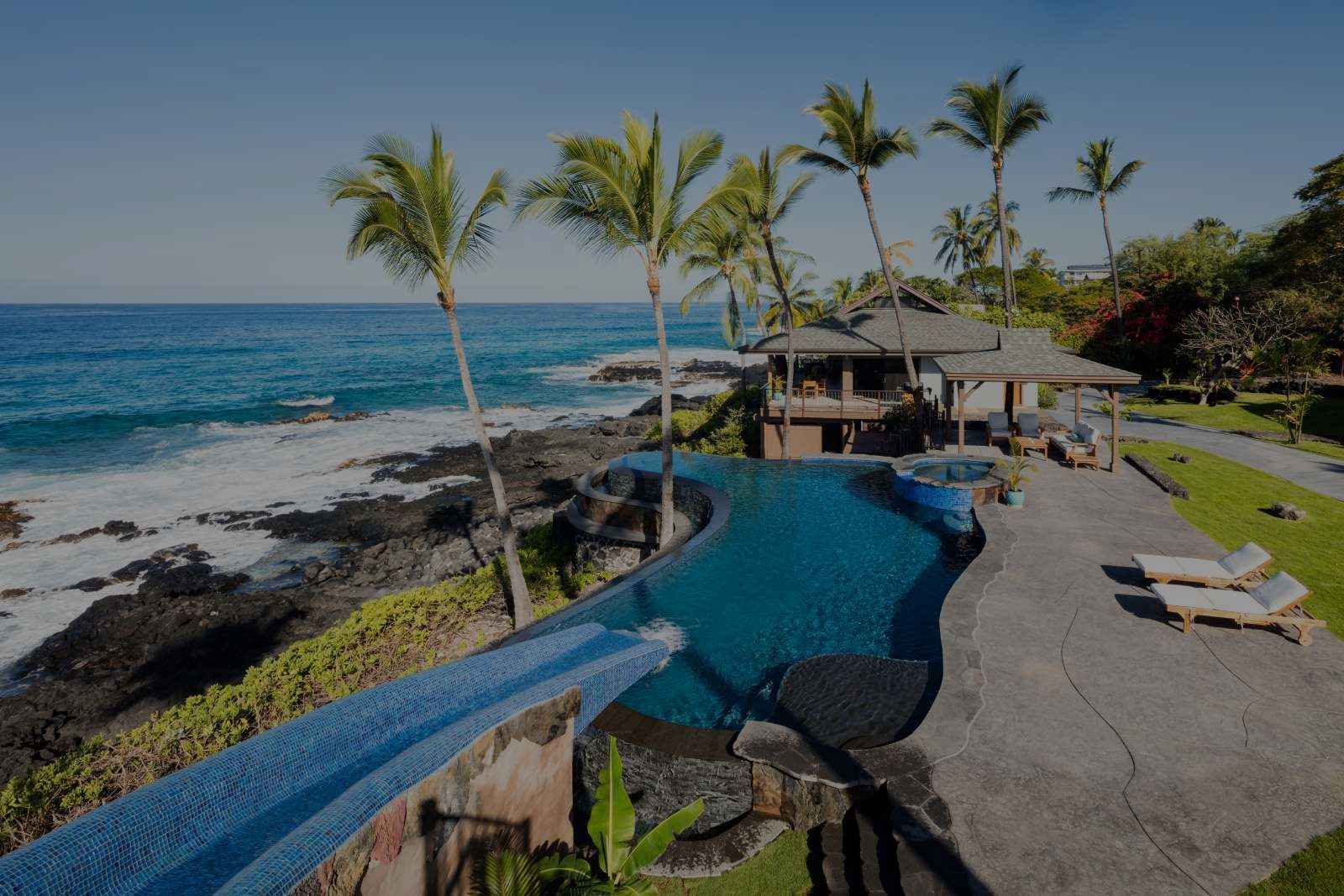 A large swimming pool surrounded by palm trees next to the ocean