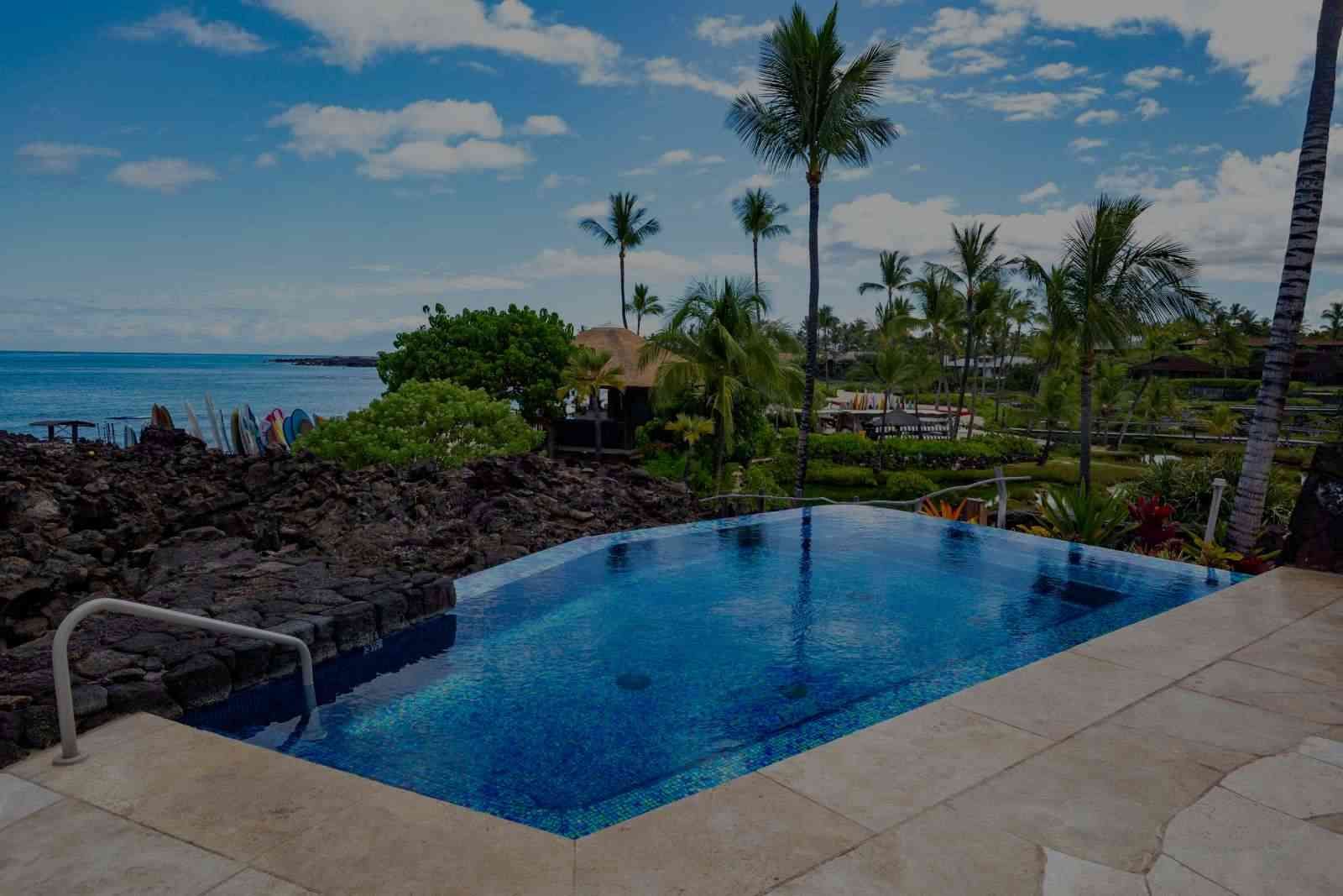 A large swimming pool with a view of the ocean and palm trees.