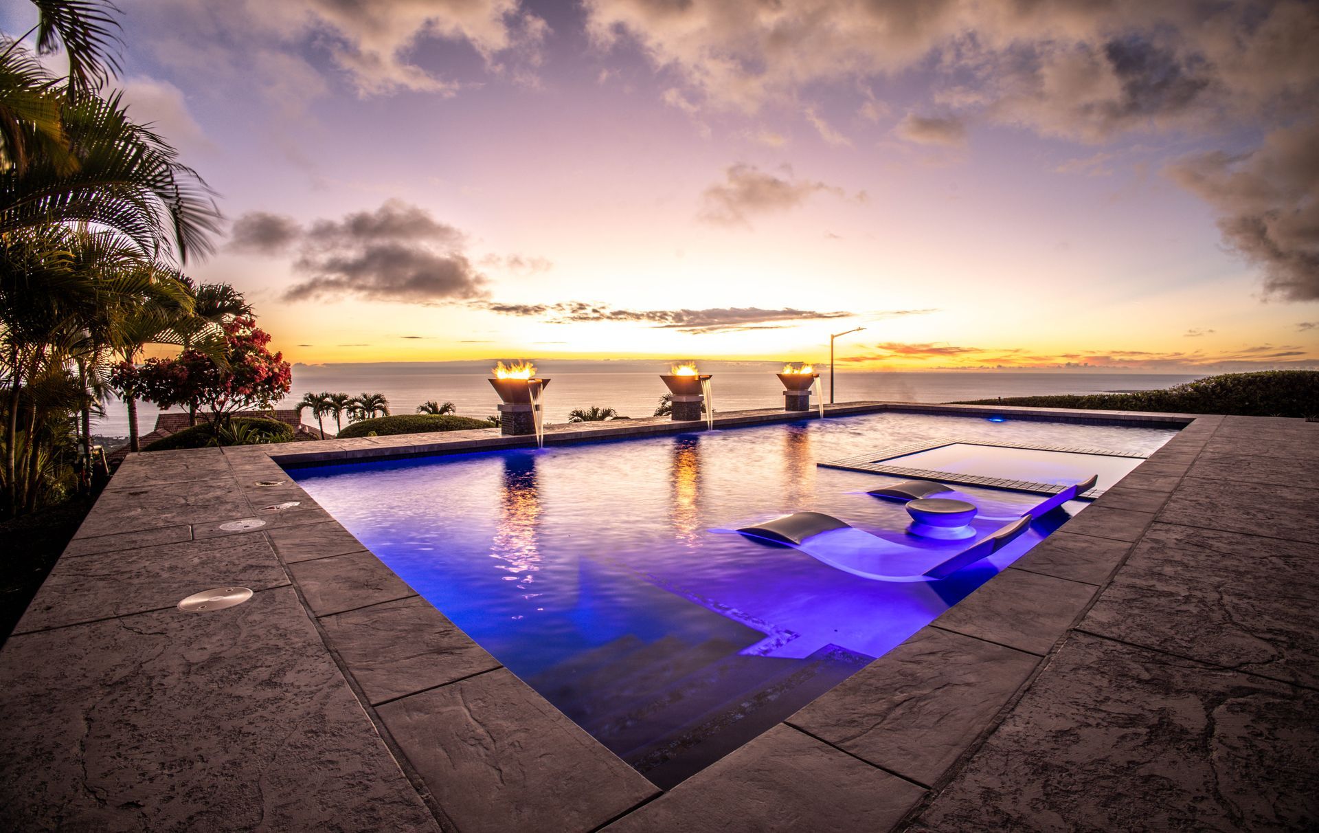 A large swimming pool with a view of the ocean at sunset.