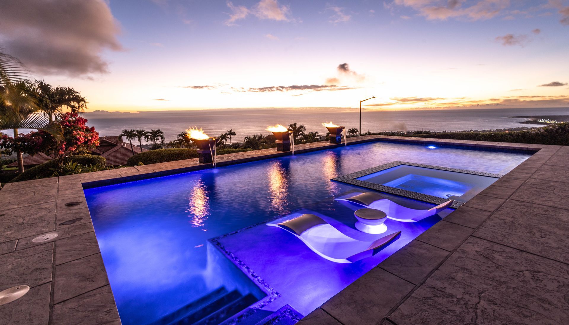 A large swimming pool with a view of the ocean at sunset.