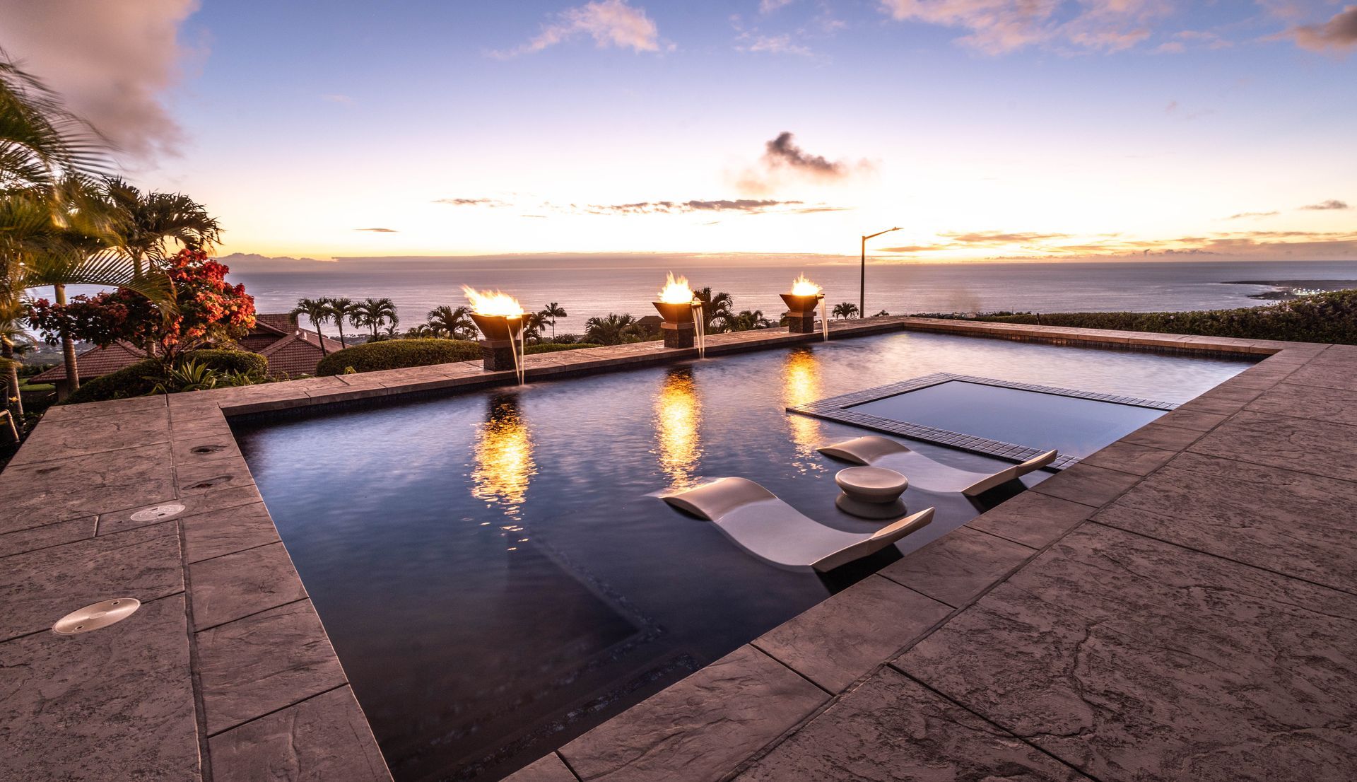A large swimming pool with a view of the ocean at sunset.