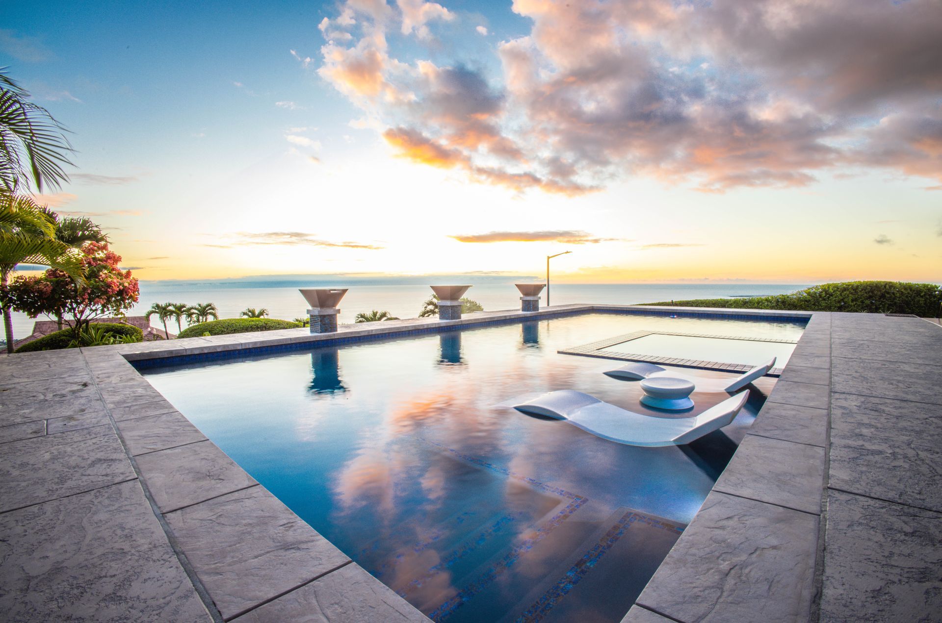 A large swimming pool with a view of the ocean at sunset.