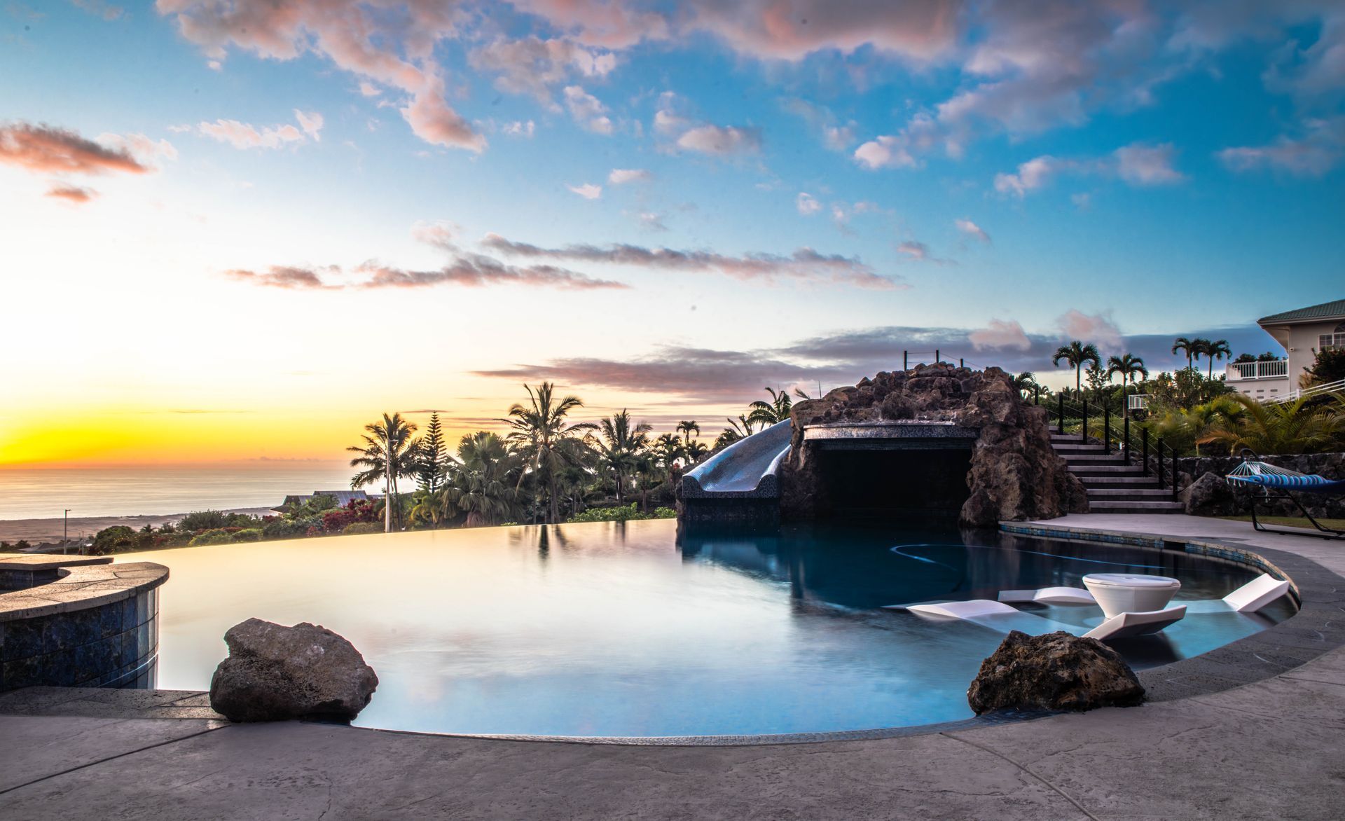 A large swimming pool with a slide and a view of the ocean at sunset.