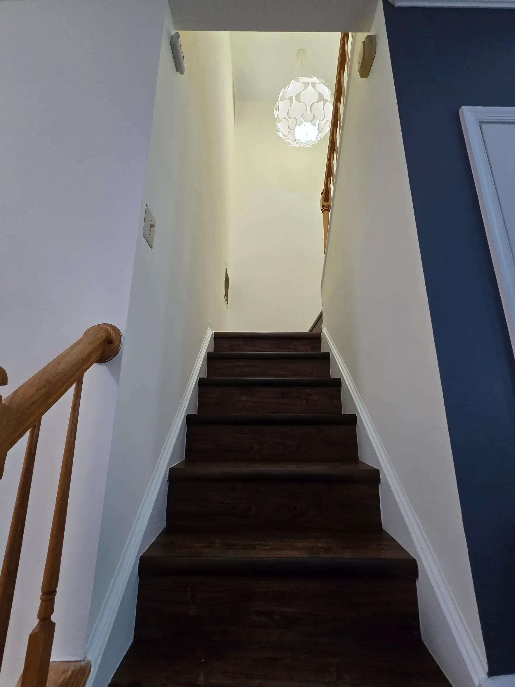Staircase leading upwards with dark brown steps, white walls, and a decorative light.