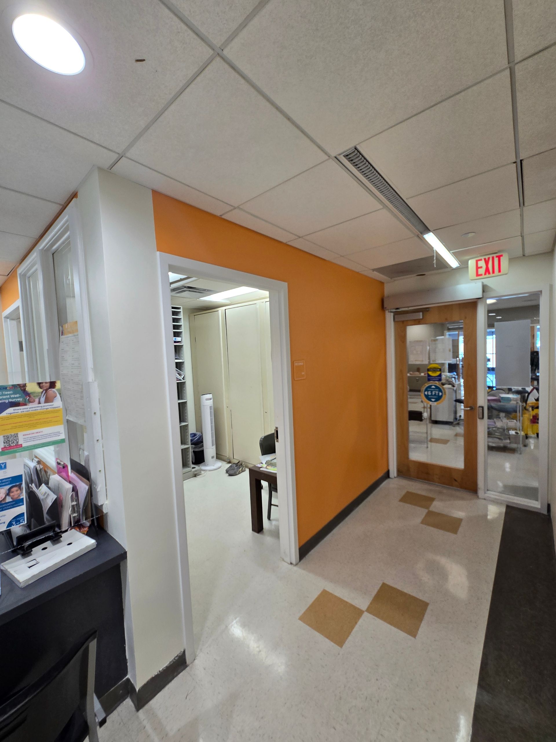 Hallway with white and orange walls, leading to a room and an exit door.