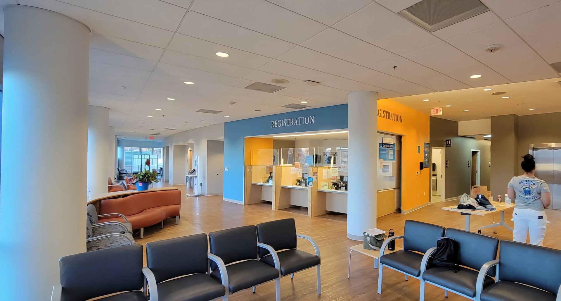 A waiting room with chairs, a reception desk, and a person standing near elevators.