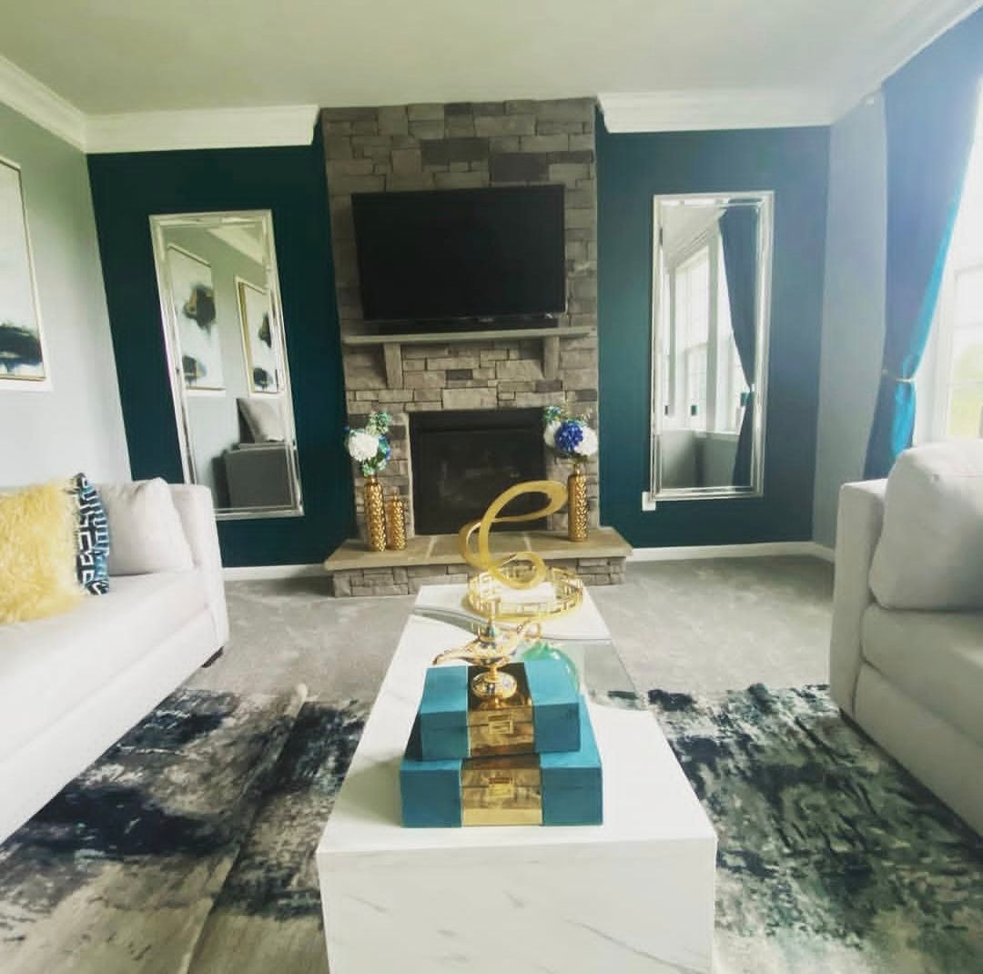 Living room with teal accent wall, stone fireplace, TV, large mirrors, white sofas, and a marble coffee table.