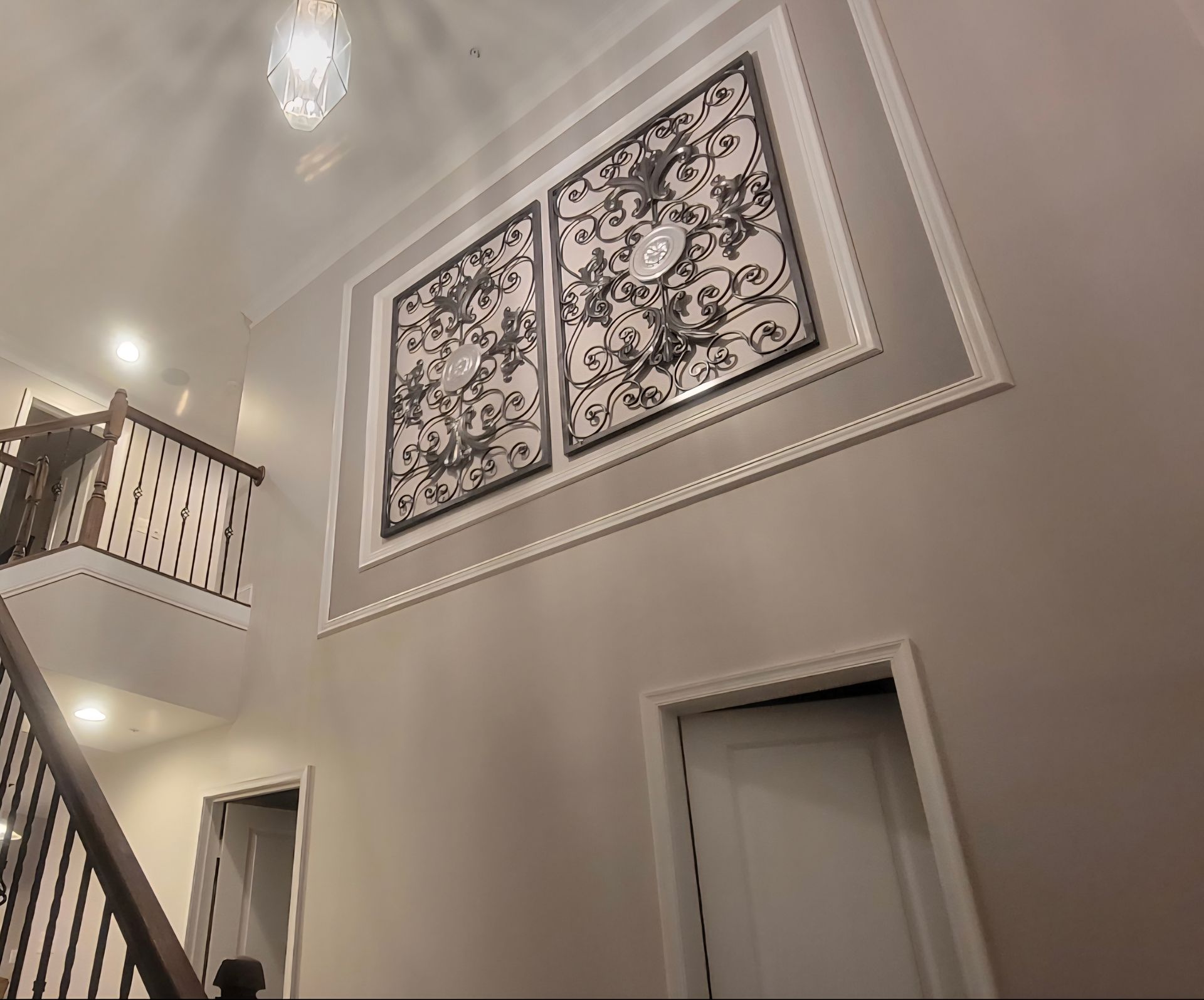 High-ceiling foyer with ornate wall art, staircase, and white trim.