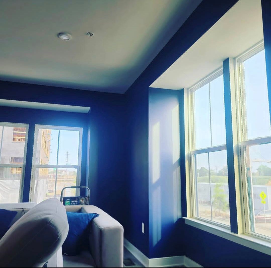 Navy blue walls frame sunlit windows in a living room, partial view of a white couch and construction site.