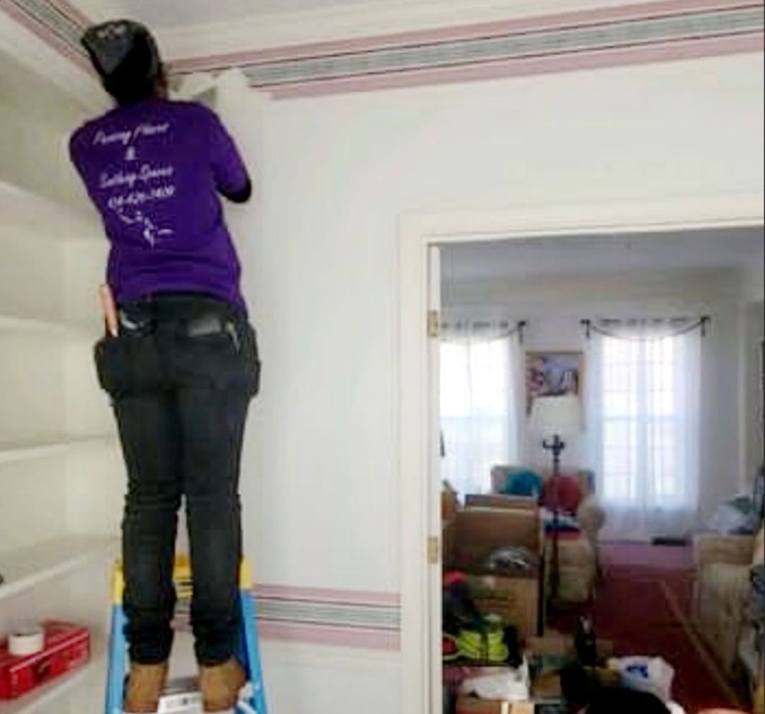 Person on a ladder removing wallpaper border in a room with a doorway to another room.