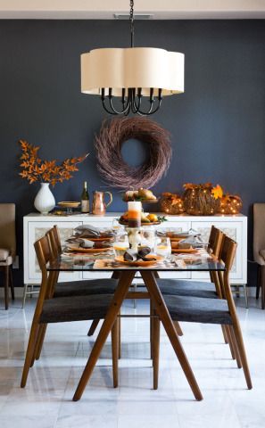 Dining room with table set for a meal. Dark wall, white buffet, wreath, and autumn decor.