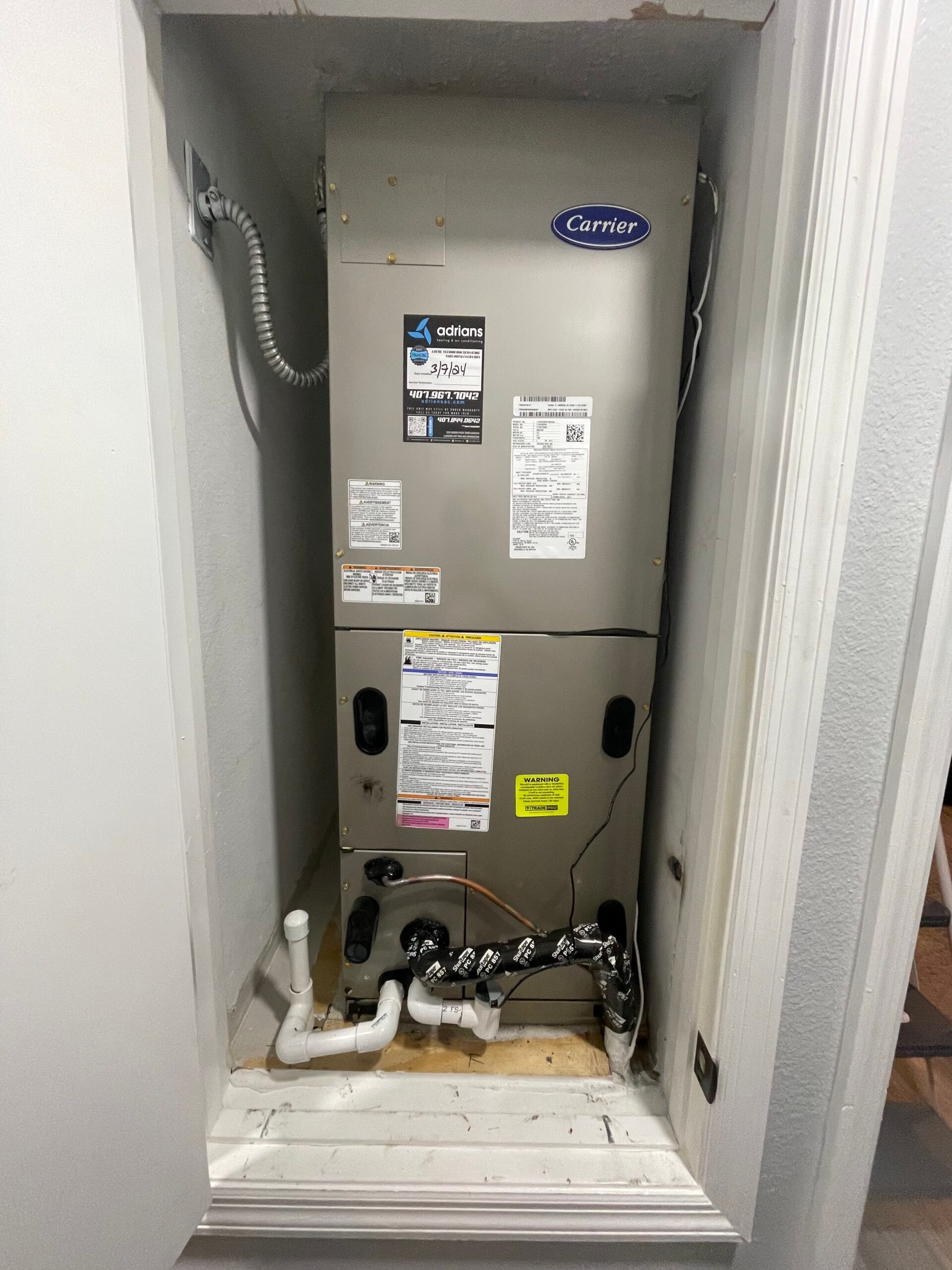 A Carrier HVAC unit installed in a closet. Gray metal with various labels and pipes at the bottom.