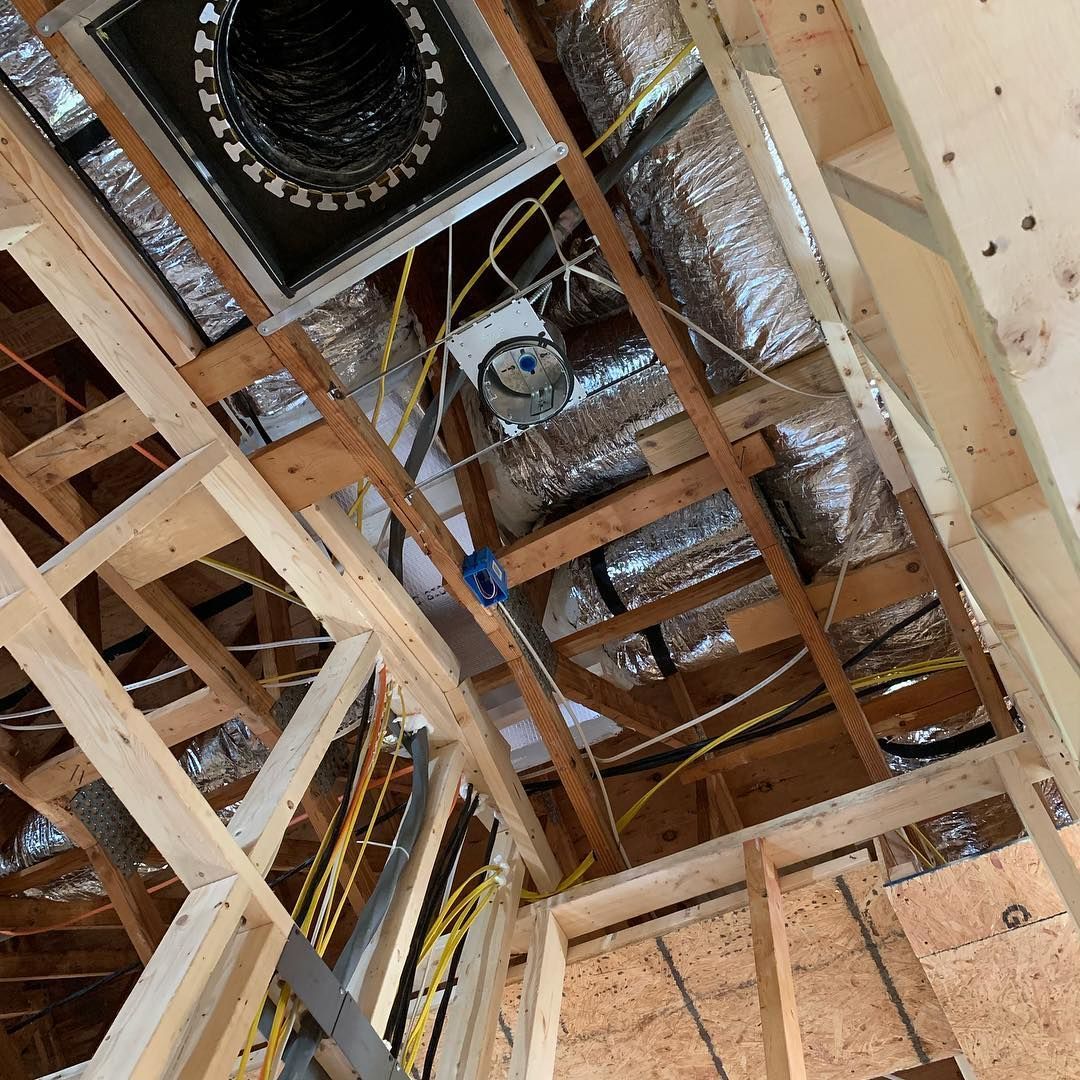 Interior view of wooden framing, ductwork, electrical wiring, and insulation in a construction setting.