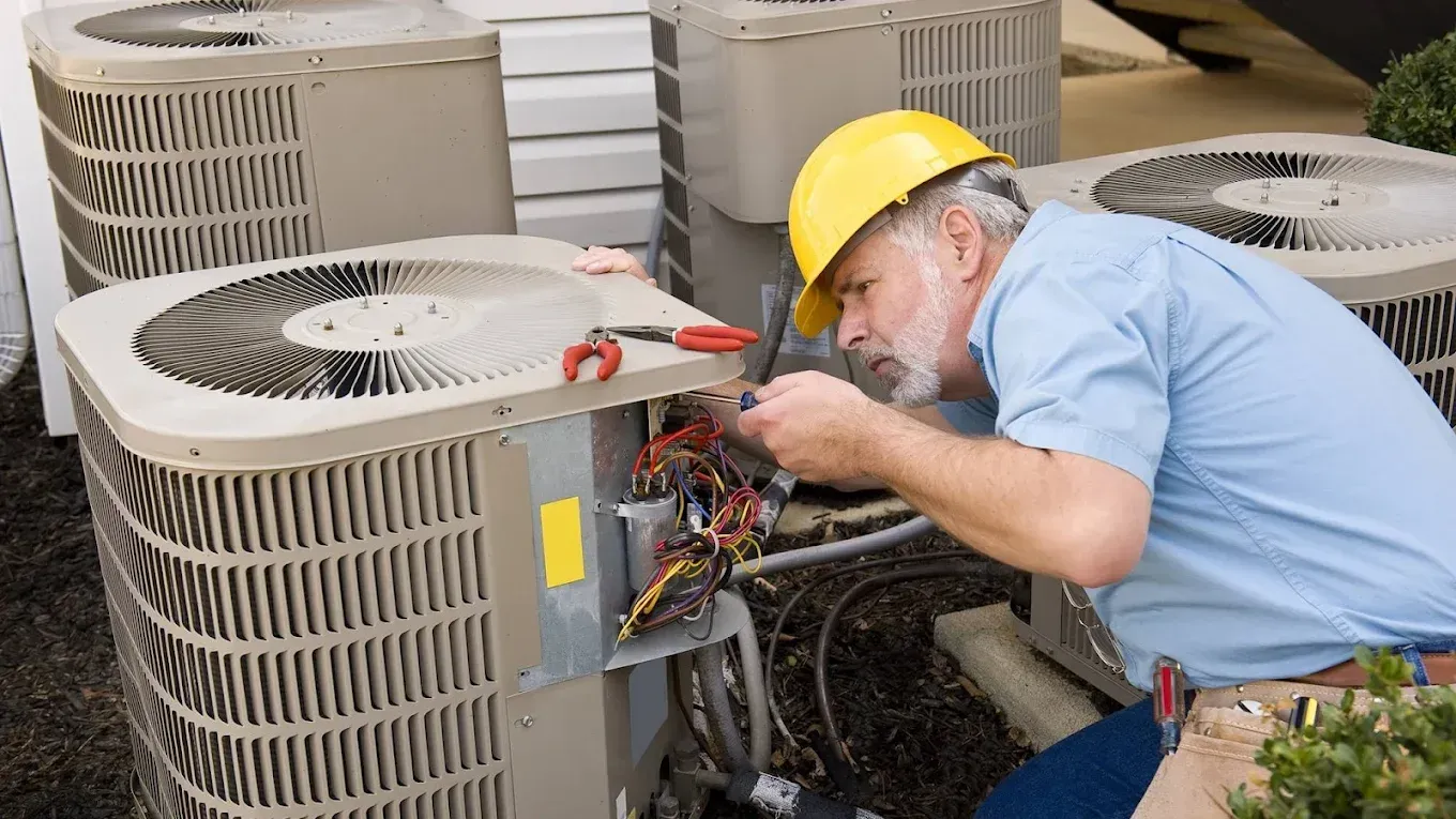 HVAC technician in yellow hard hat working on an air conditioning unit.