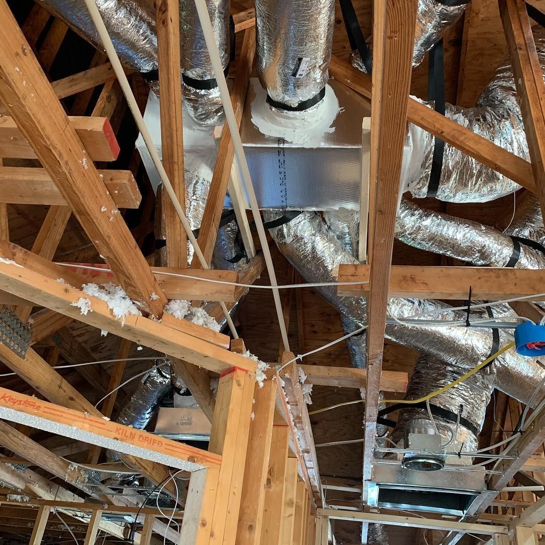 Wooden attic with exposed beams and HVAC ductwork wrapped in silver insulation.