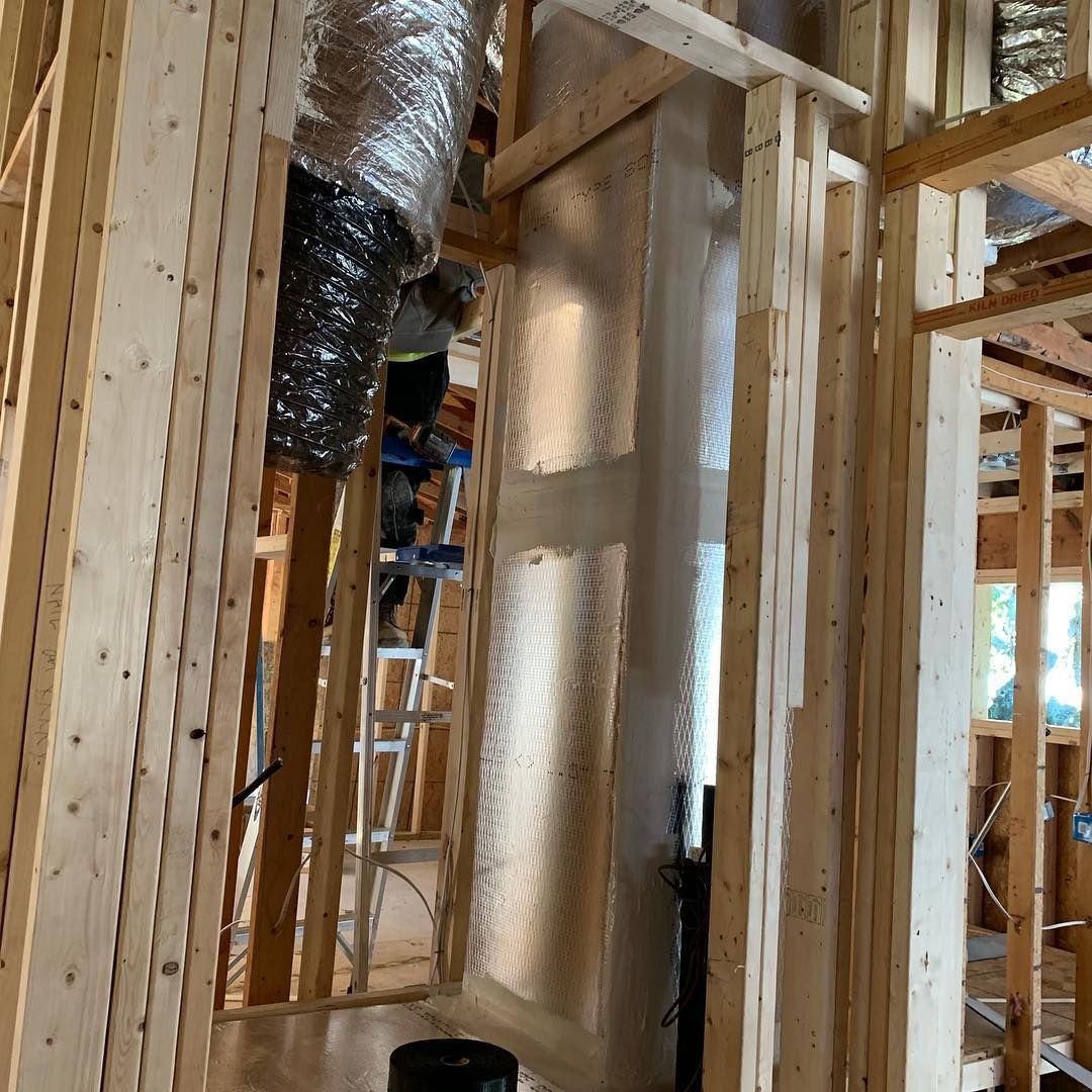 Interior of a house under construction; wooden framing, insulation, ductwork, and ladder visible.