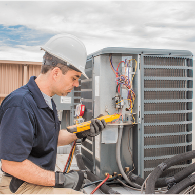 HVAC technician in hard hat inspects air conditioner unit on rooftop with testing tool.
