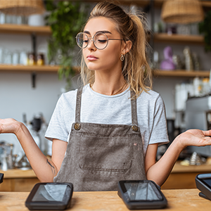 Woman behind counter shrugs, palms up, looks confused; two payment terminals sit in front of her.