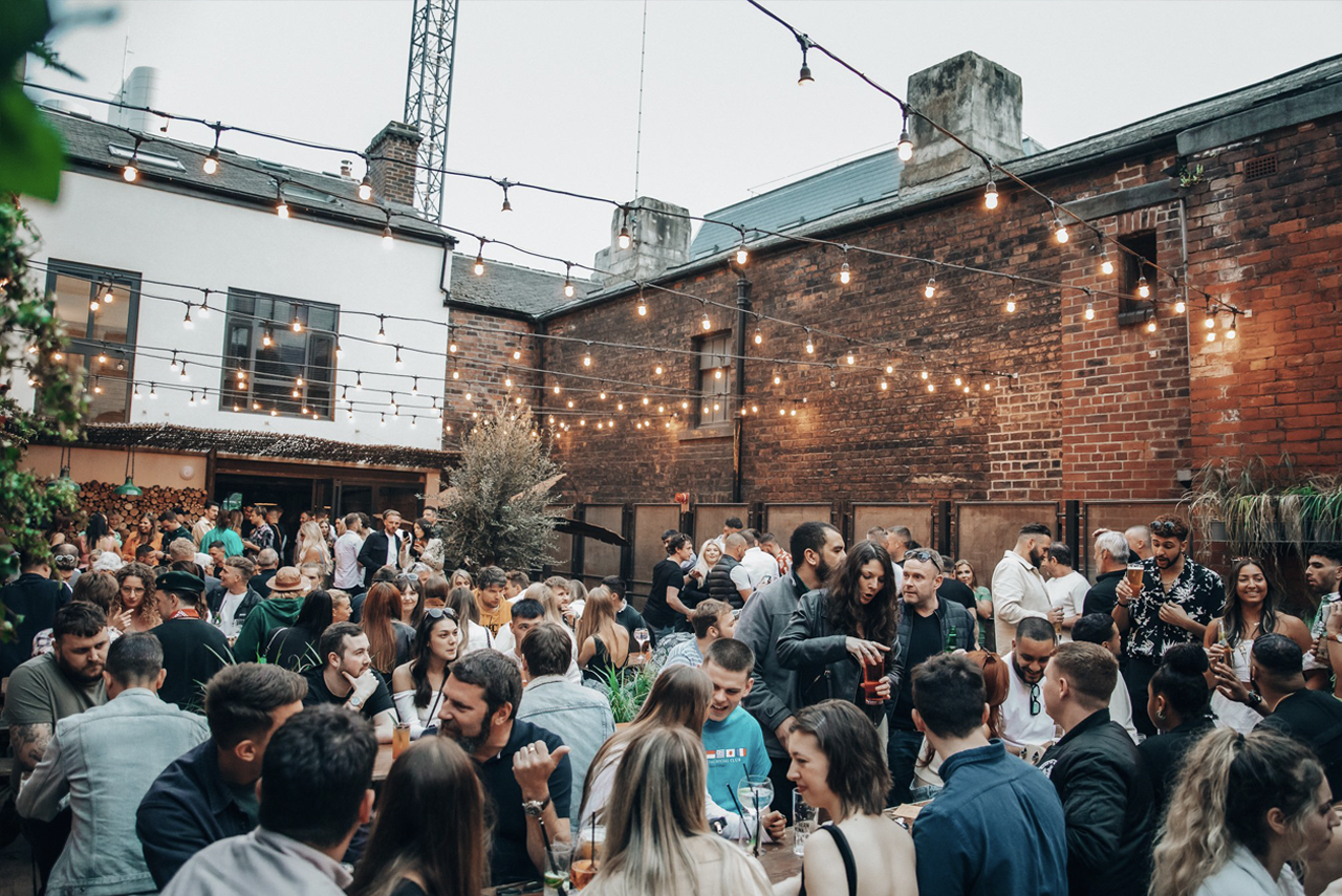 A busy outdoor area of a bar, with lots of people sat at tables enjoying themselves