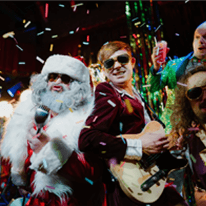 Santa Claus holding a microphone while stood next to a man playing guitar. 