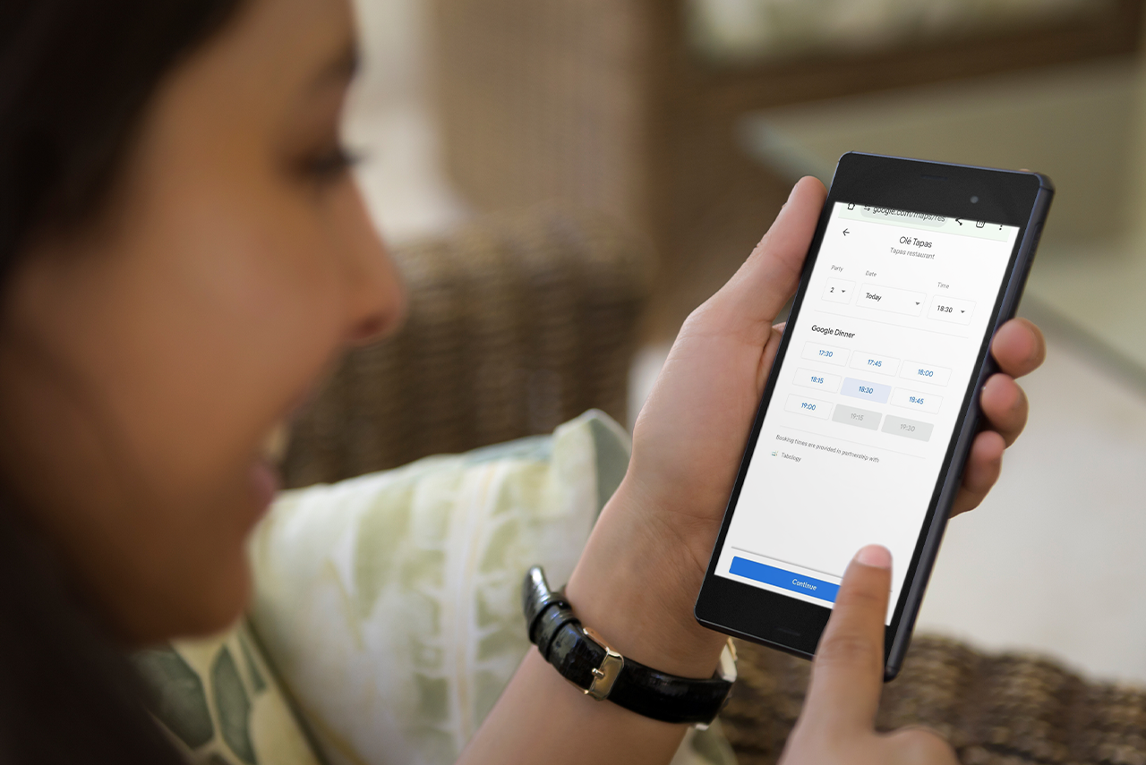 Woman using a smartphone, smiling. She is using Reserve with Google to book a table at a restaurant.