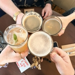 Four people toasting drinks: beer, cocktail. Close up shot.
