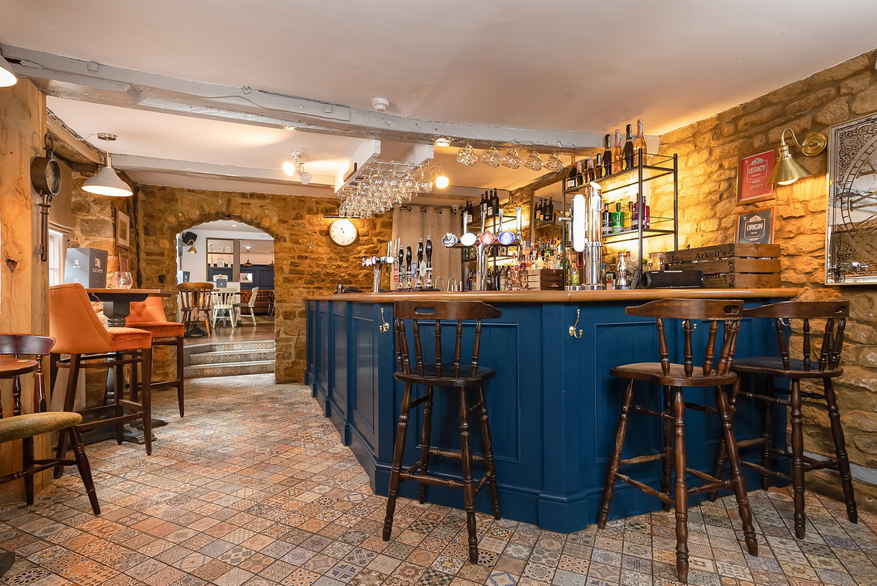 Interior of a pub with a blue bar, wooden stools, and stone walls.