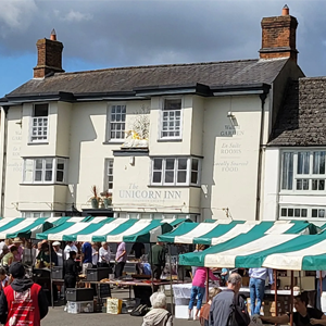 Market stalls with green and white striped canopies in front of the Unicorn Inn building. People browse the stalls.