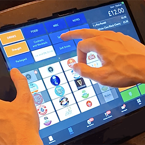 Hands using a colorful touchscreen restaurant ordering kiosk with menu tiles and price displayed.
