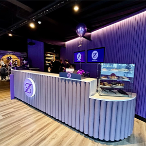 Purple-themed café counter with display case and wall screens in a modern indoor venue