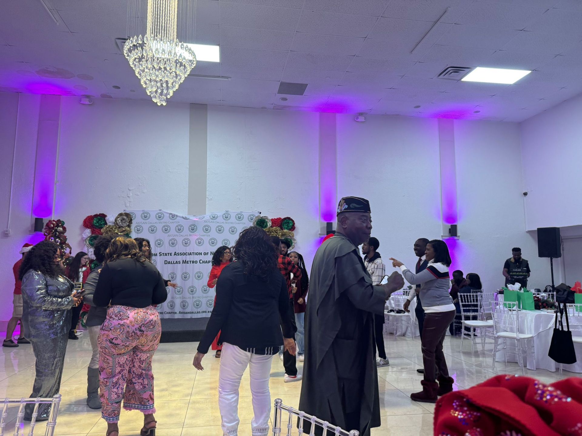 A group of people are dancing in a large room with purple lights.