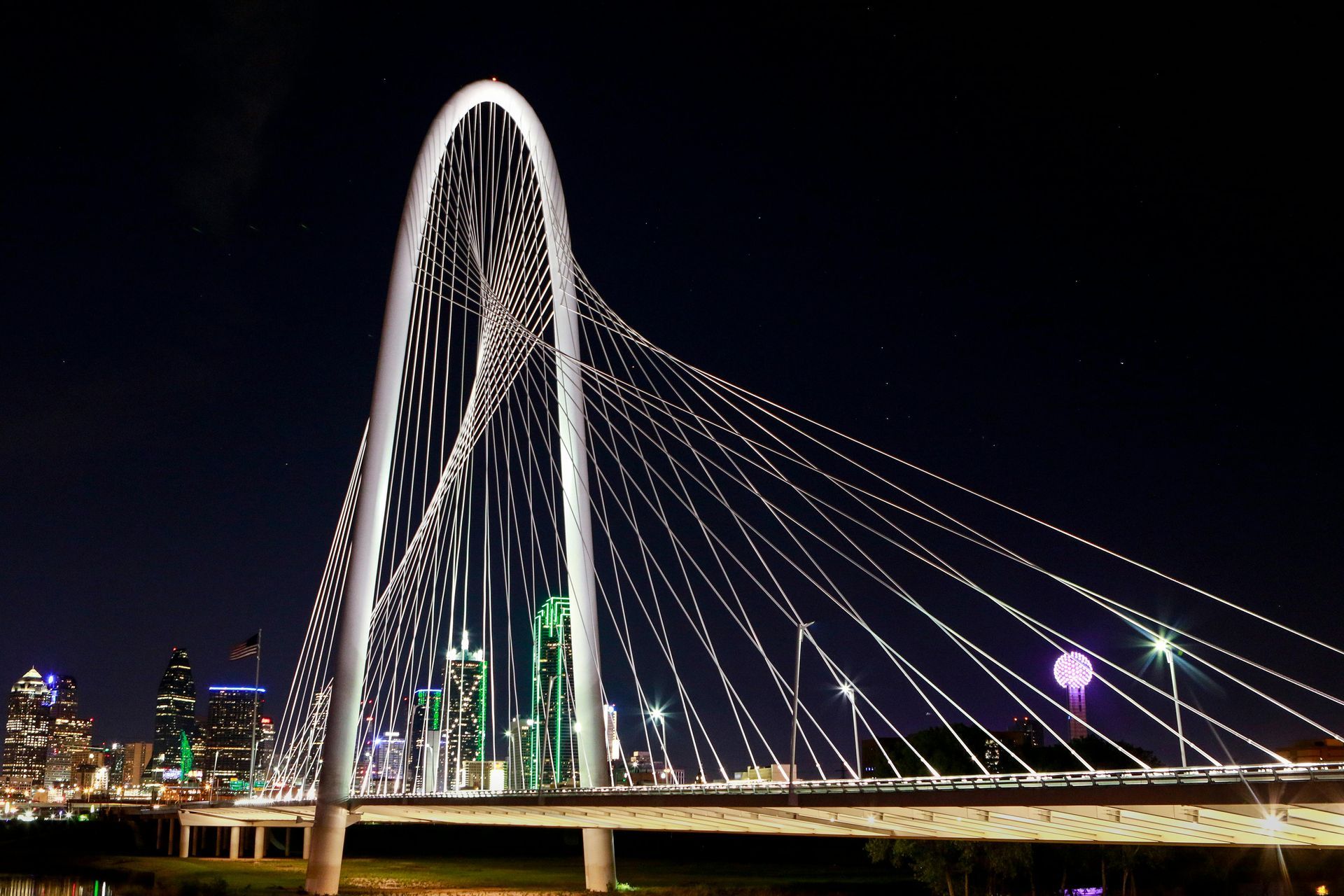 A bridge is lit up at night with a city in the background
