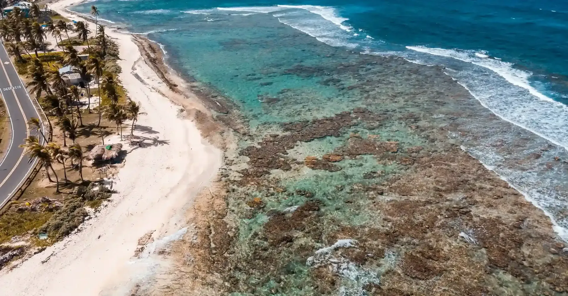 Vista aérea de las aguas cristalinas, donde se observan arrecifes de coral y la costa de la isla. La playa de San Andrés está rodeada por el mar turquesa, tono característico de este destino caribeño.