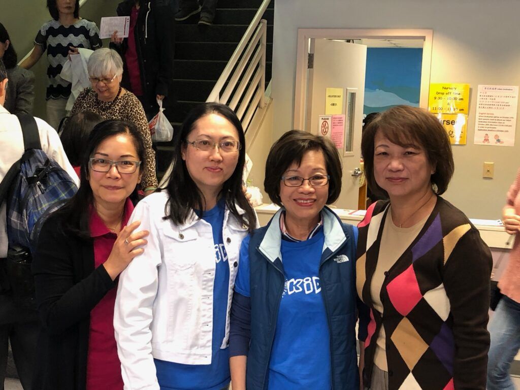 Four people stand together indoors, smiling for a photo in a casual office or event setting.