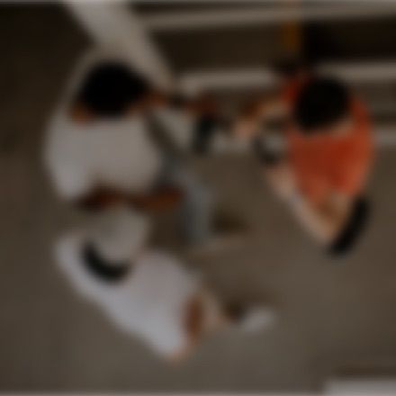 Three people sit at a table, viewed from above, with one person wearing an orange shirt and two in white.