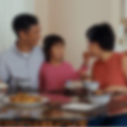 A family sits together at a dining table, having a meal in a brightly lit room.