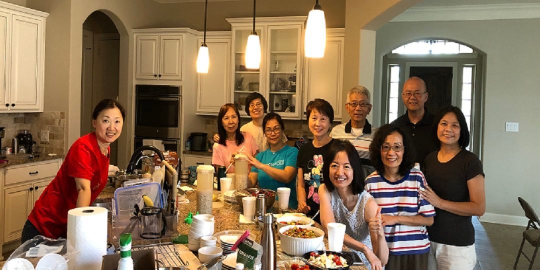 A group of people standing together in a kitchen around a large island, smiling at the camera during a gathering.