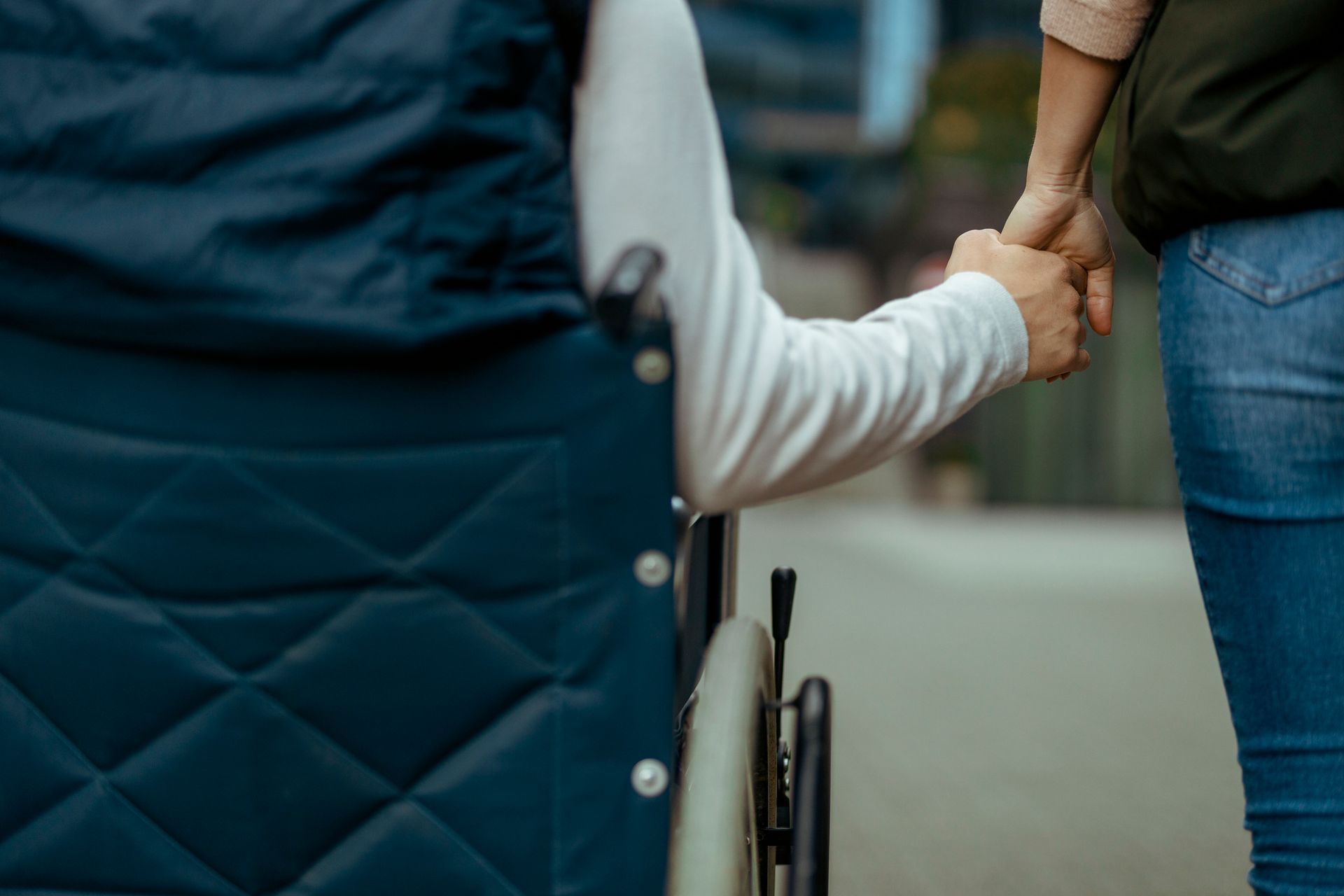 Due persone che si tengono per mano, una accanto a una sedia a rotelle, all'aperto.