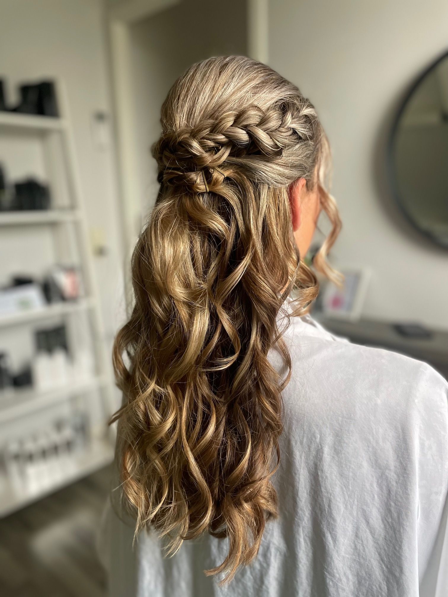 Vrouw met golvend blond haar, half opgestoken met een vlecht bovenop, draagt ​​een witte blouse.