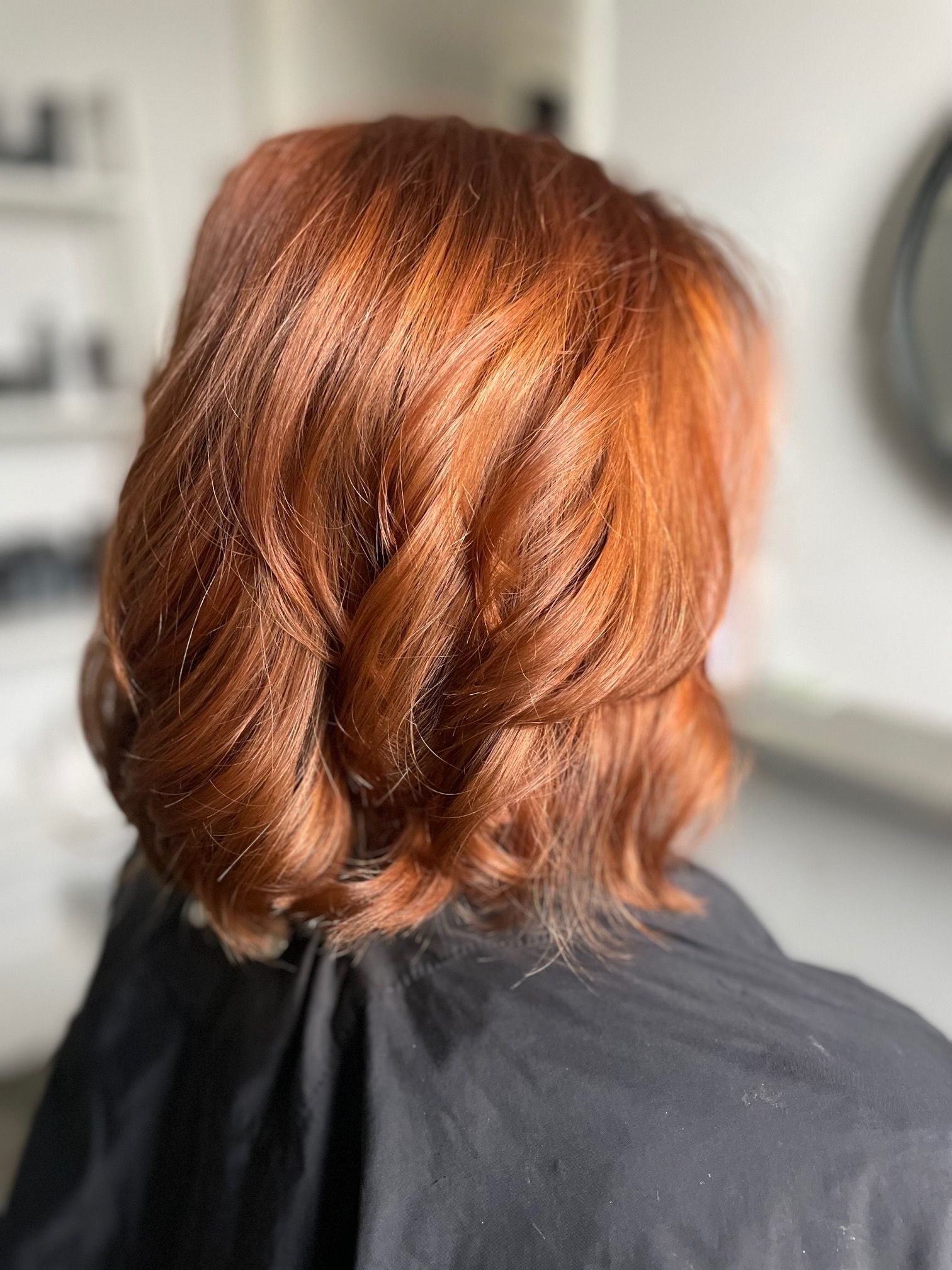 Vrouw met koperkleurig, golvend bobkapsel in een kapsalon, gekleed in een zwarte cape.