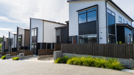 Row of modern townhouses with white and black siding, wooden fences, and greenery.
