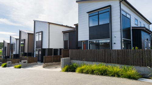 Row of modern townhouses with white and black siding, wooden fences, and greenery.