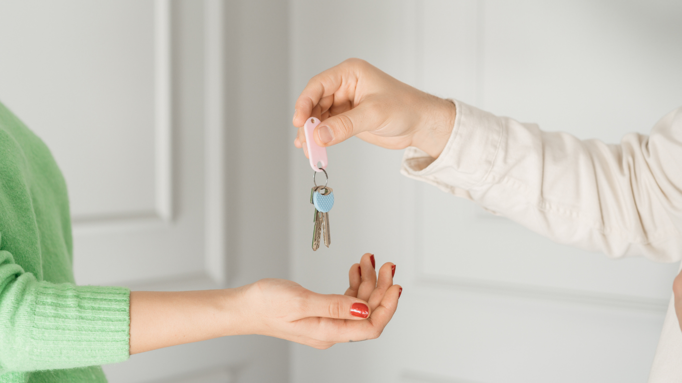 A person's hand giving keys to another person. The person receiving keys is wearing a green shirt.