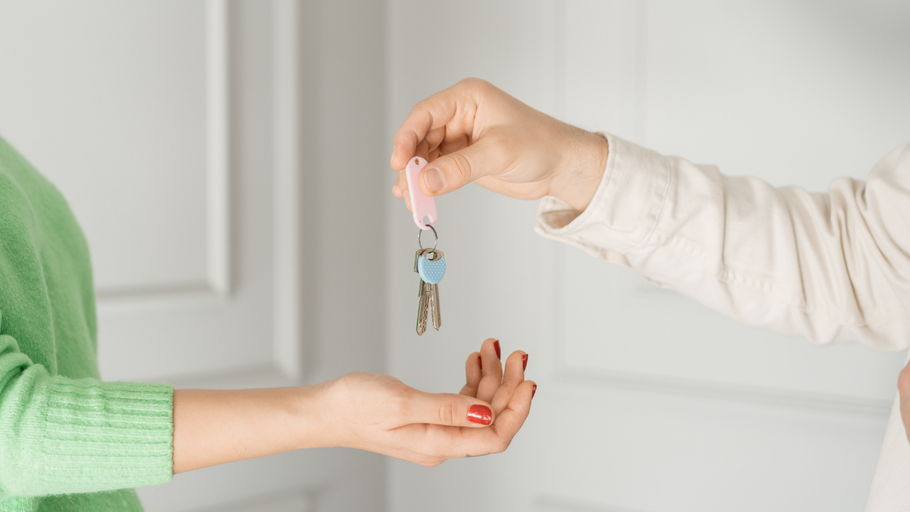 A person's hand giving keys to another person. The person receiving keys is wearing a green shirt.