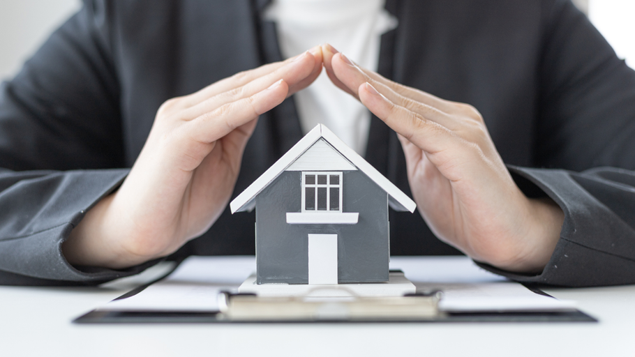 Hands cupped over a miniature gray house, symbolizing protection.