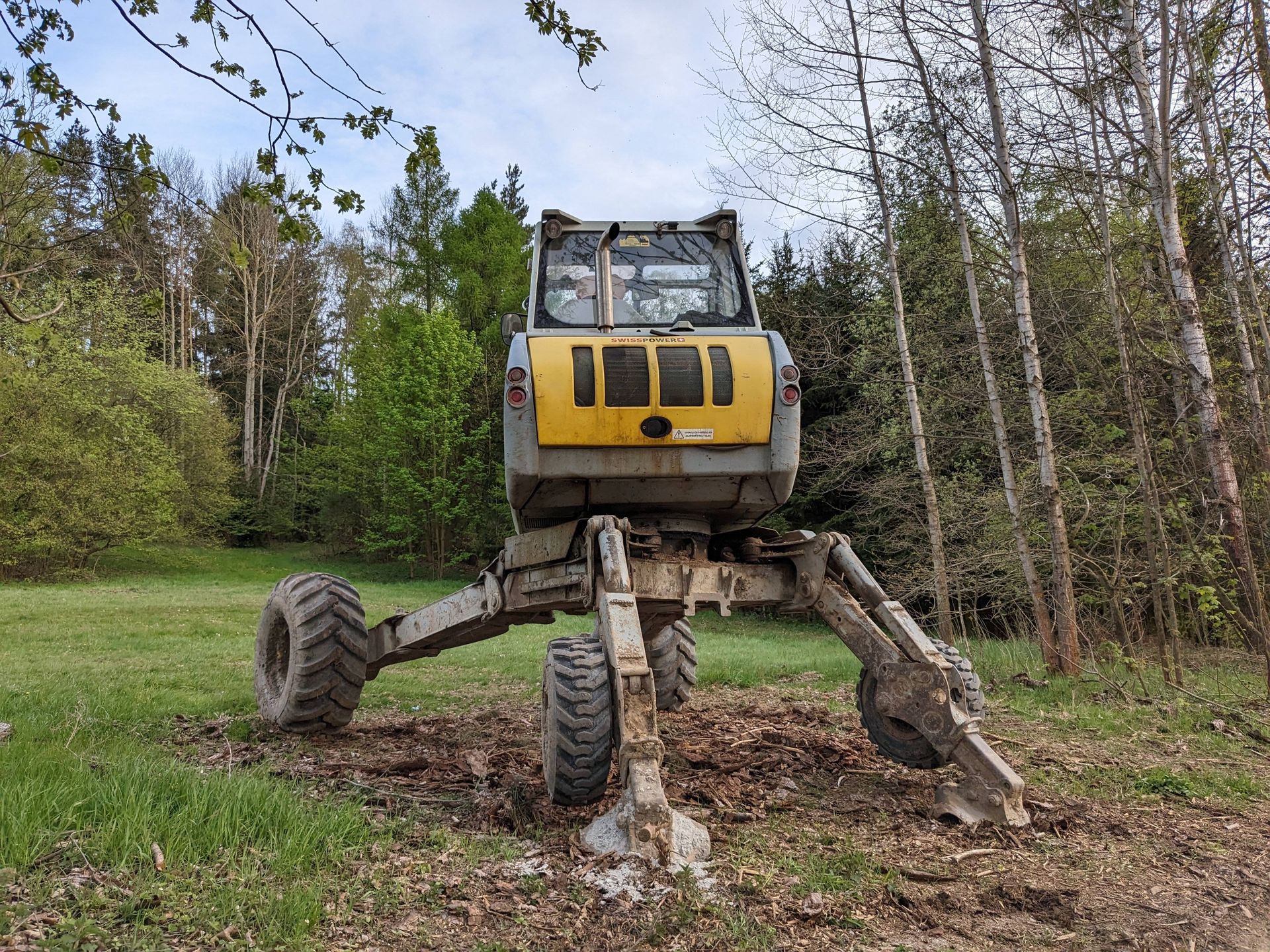 A yellow excavator is moving a pile of dirt in a yard.