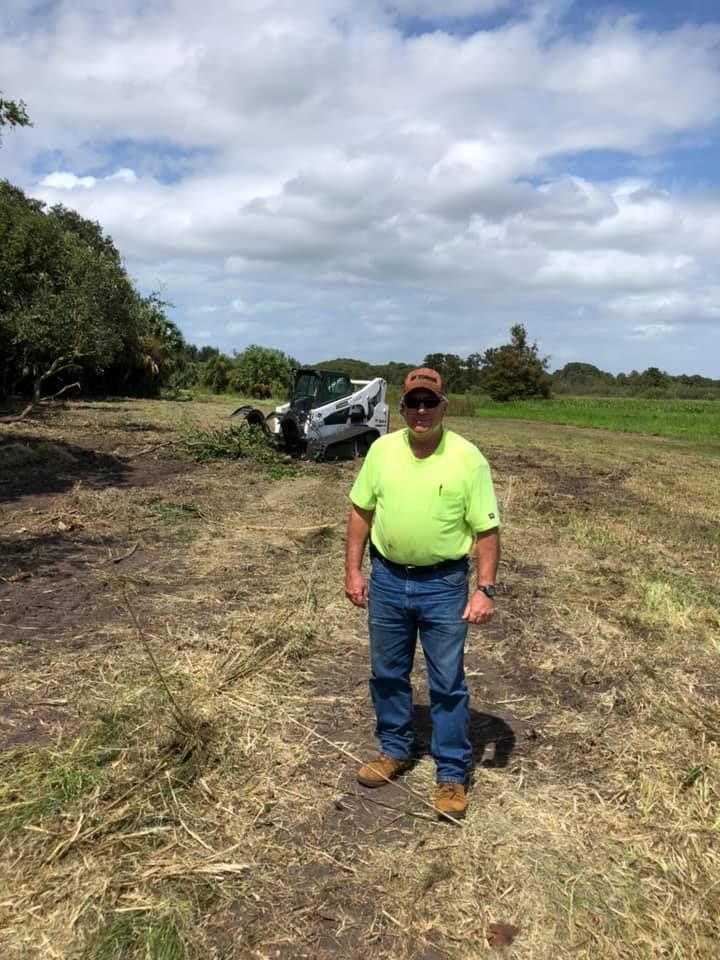 A man is standing in a field with a bulldozer in the background.