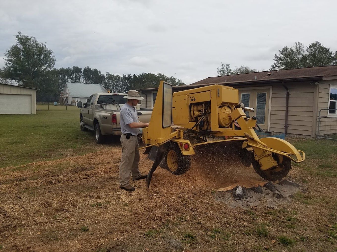 A man is working on a stump grinder in front of a house