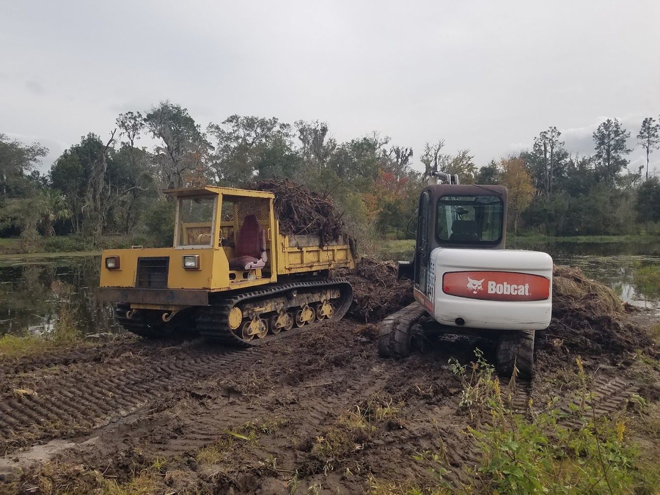 A bulldozer and a dump truck are driving through a muddy field.